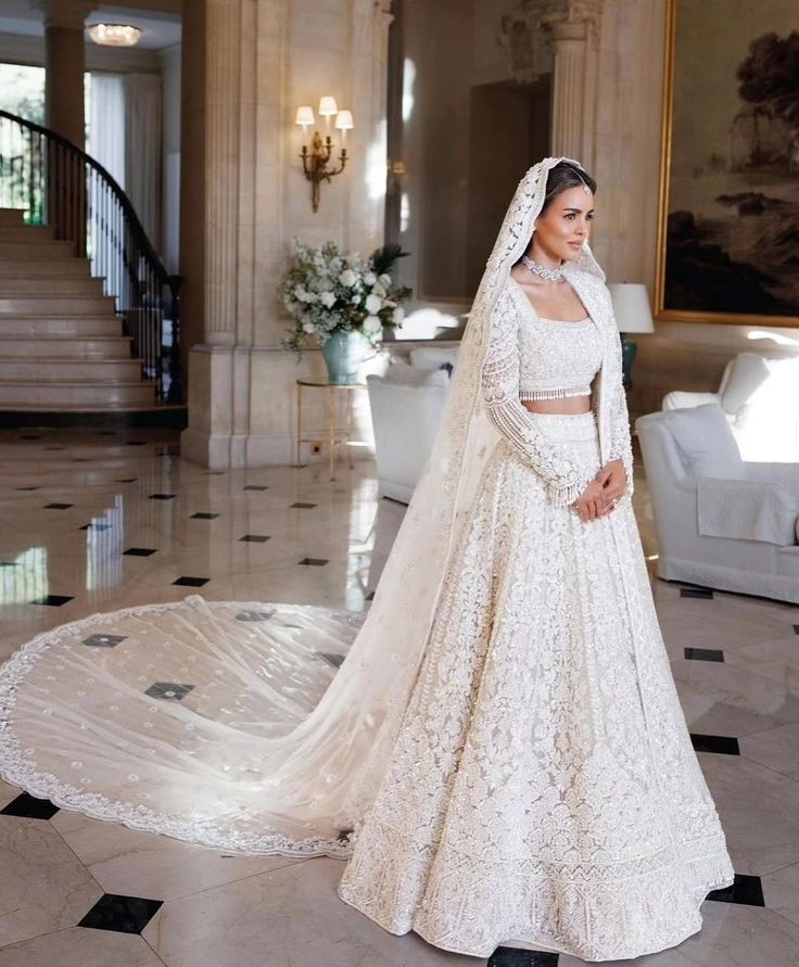 a woman in a white wedding gown and veil standing on a marble floor next to stairs