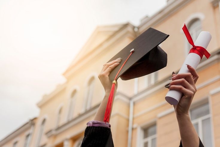 two people in graduation caps and gowns hold up their mortares to the sky