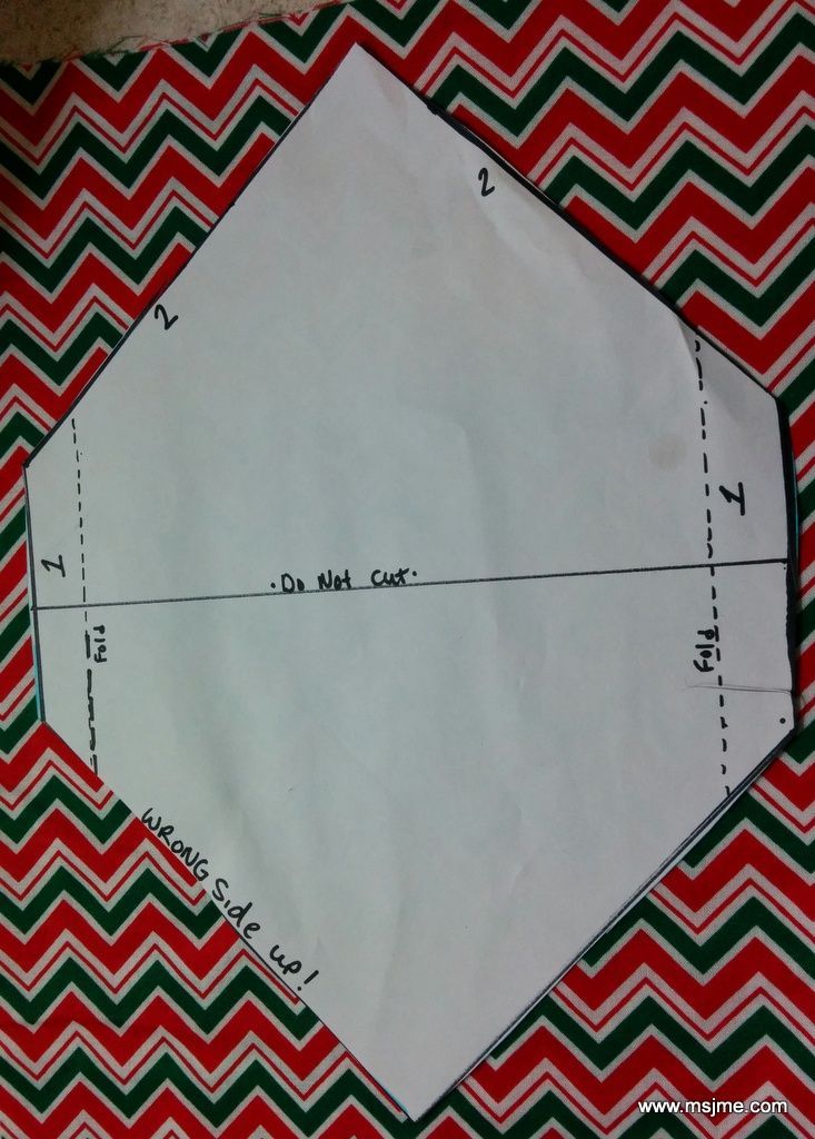 a piece of paper with the end cut out on top of red and green chevroned fabric