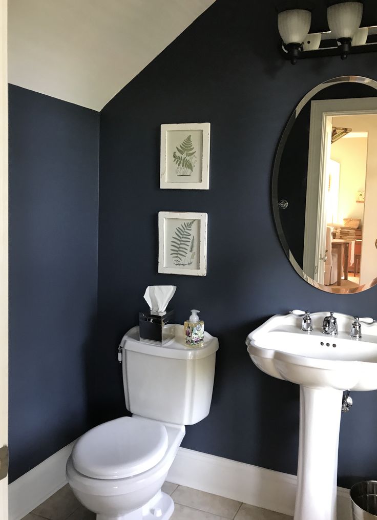 a white toilet sitting next to a sink in a bathroom under a large round mirror