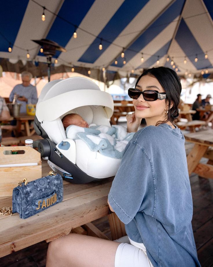 a woman sitting at a table with a baby in a car seat on top of it