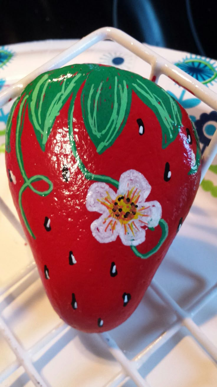 a painted strawberry sitting on top of a white plate next to a green and blue flower