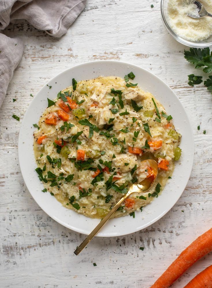 a white bowl filled with food next to carrots and parsley on a table