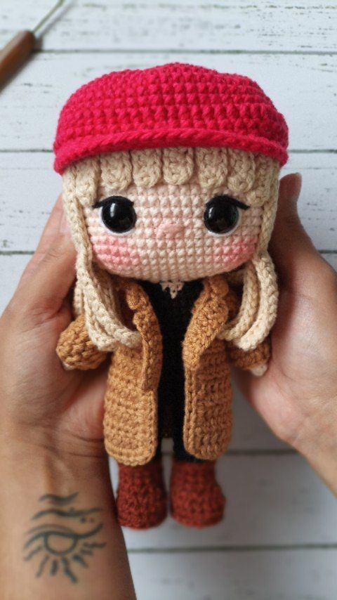 a hand holding a small doll with a red hat and coat on it's head