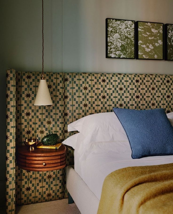 a bed with white sheets and blue pillows in a bedroom next to two pictures on the wall