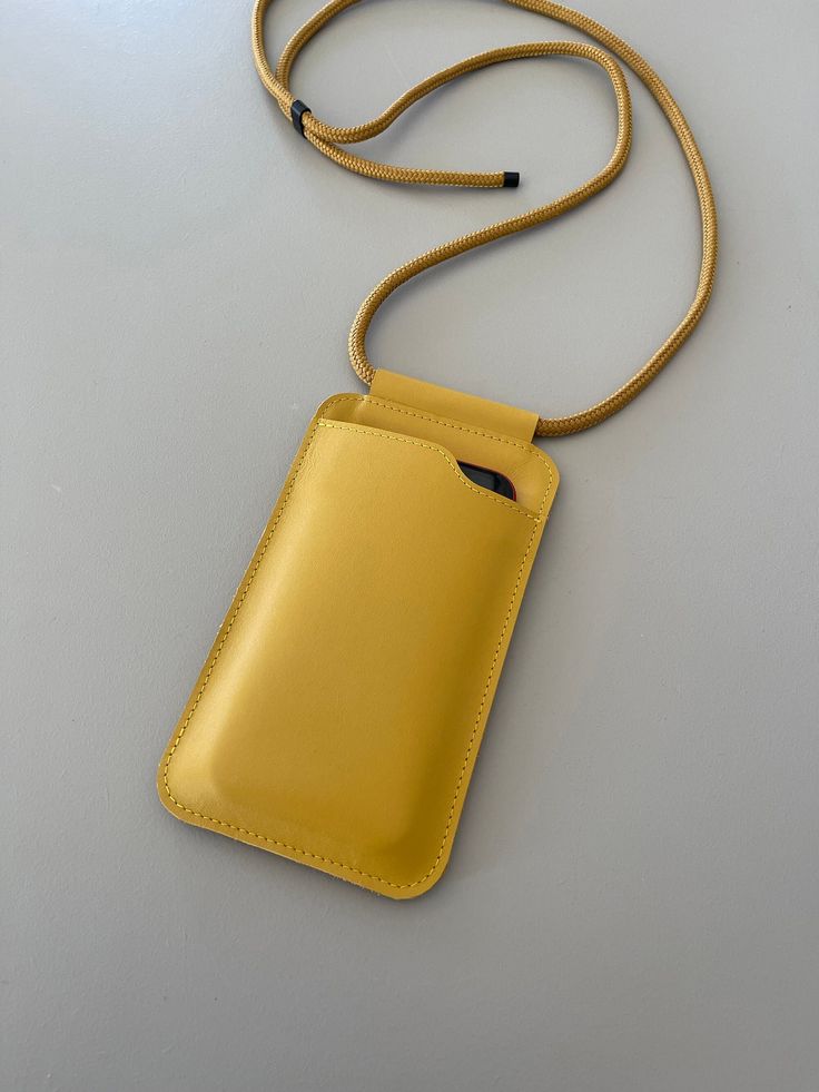 EDGE phone sling is a minimalist small bag / cover for your phone.   width: 10,5 cm / 4.1 in  height: 18 cm / 7.1 in * zipper pocket for cards, key or lipstick at the back * shoulder strap made of high quality PPM cord, finished with metal end caps * the metal slider tube makes it easy to adjust the shoulder strap * made for the iPhone 12 and 12 pro max but any phone of the same size or smaller will fit * designed & handmade by Marieke Jacobs in the Netherlands This product is made with the greatest care using genuine leather. Because every product is made by hand, small irregularities can occur. Please take into account that leather can contain small imperfections, as they are part of its beauty. Leather is a natural material and should be treated with love! Portable Yellow Phone Bag For Everyday Use, Yellow Rectangular Phone Bag For Everyday, Yellow Crossbody Phone Bag For Travel, Yellow Travel Crossbody Phone Bag, Trendy Yellow Phone Bag For Daily Use, Rectangular Gold Mobile Phone Bag, Gold Rectangular Phone Case, Yellow Rectangular Phone Bag For Everyday Use, Yellow Crossbody Phone Bag With Cell Phone Pocket