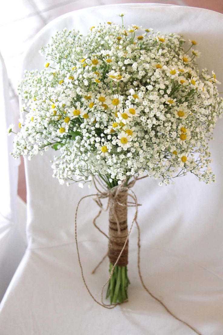 a bouquet of daisies tied to a white chair with twine on the back