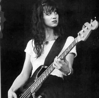 black and white photograph of a woman playing a bass guitar in front of a microphone