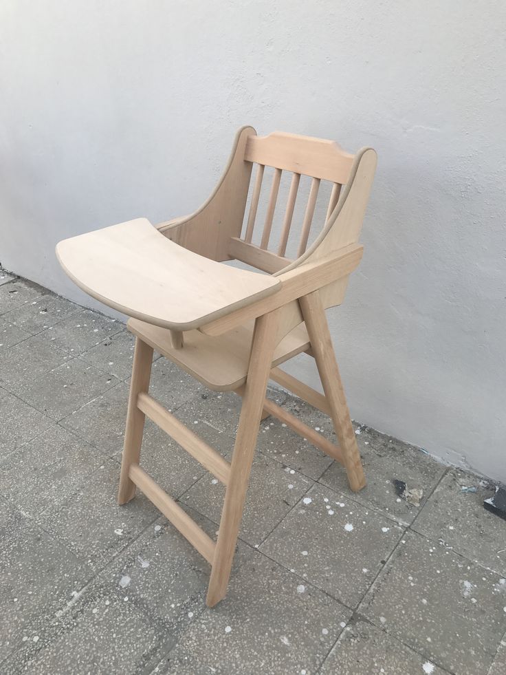 a wooden chair sitting on top of a sidewalk next to a white wall and cement floor