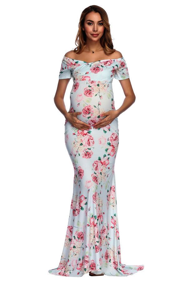 a pregnant woman in a floral print gown with her hands on her hips, posing for the camera