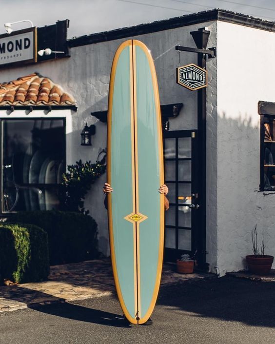 a man standing in front of a building holding a surfboard