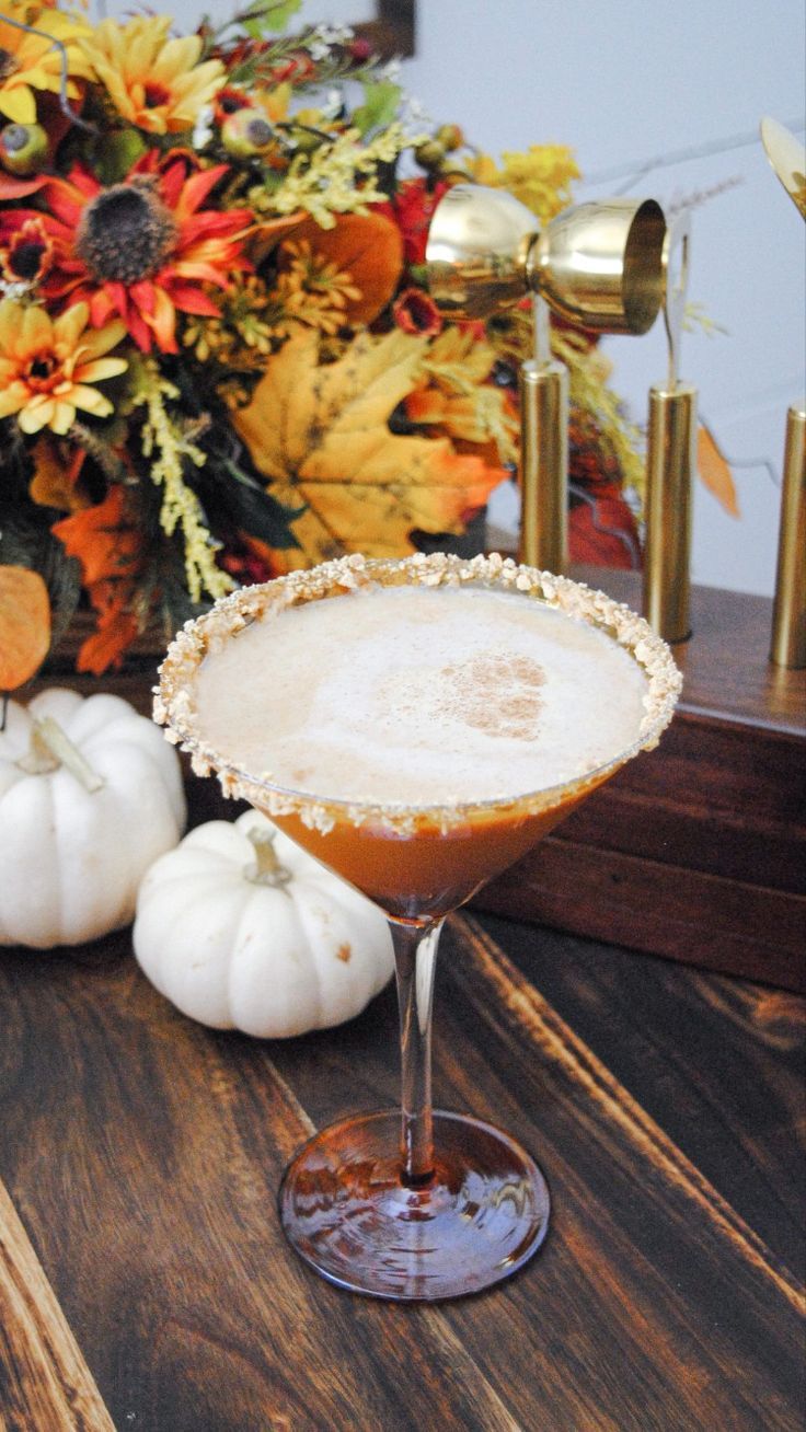 a cocktail sitting on top of a wooden table next to white pumpkins and flowers