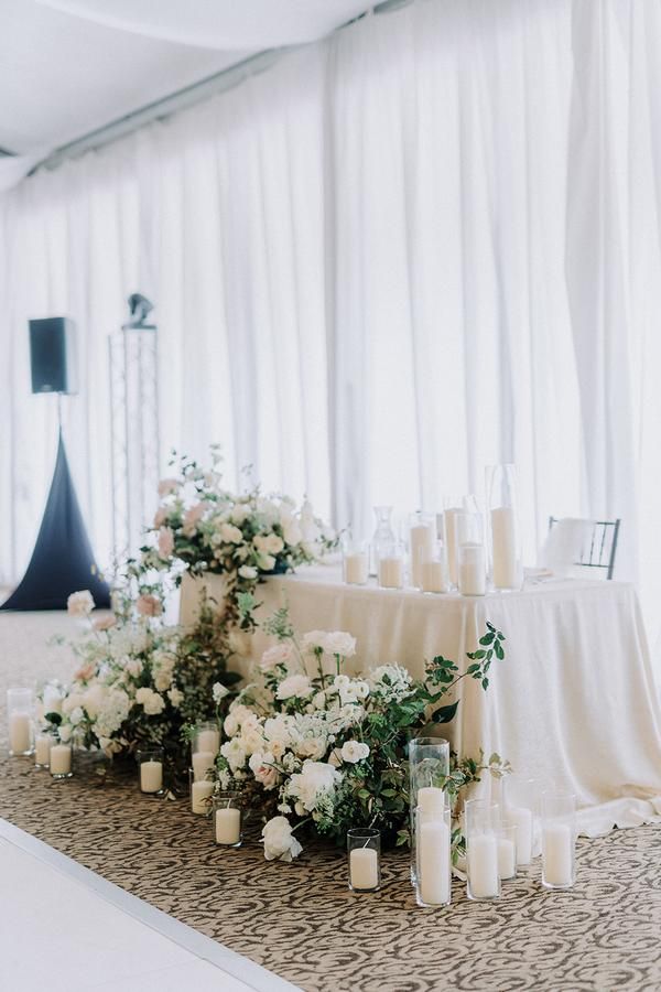 the table is set up with candles and flowers for an elegant wedding reception in front of white drapes