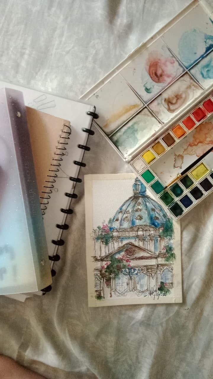 an artist's notebook and watercolors are sitting on a bed