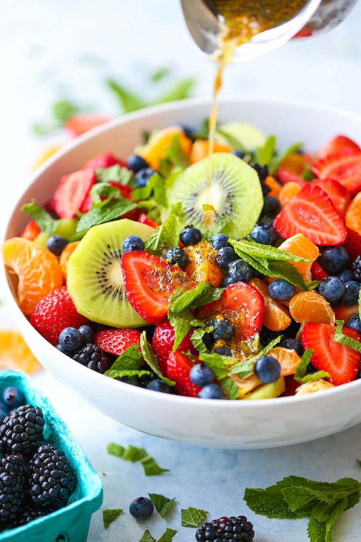 a white bowl filled with fruit salad and dressing being drizzled over it