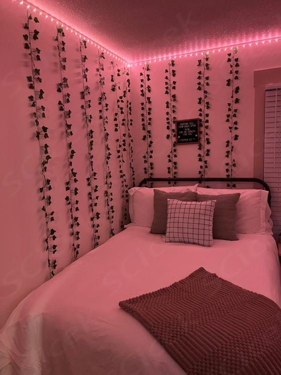 a bed in a room with pink walls and lights on the headboard is decorated with ivy vines