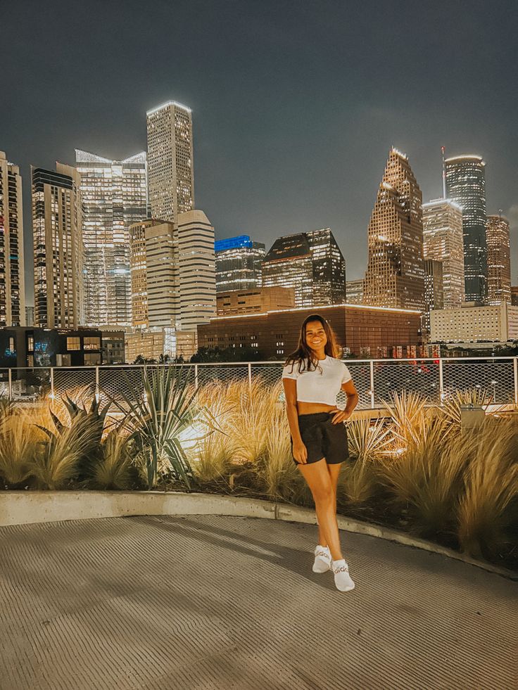 a woman standing in front of a cityscape with tall buildings and grass on the ground