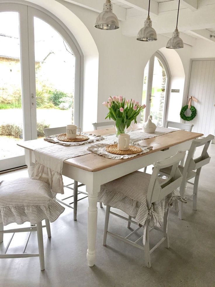 a dining room table and chairs with flowers in vases on the top, next to an arched window