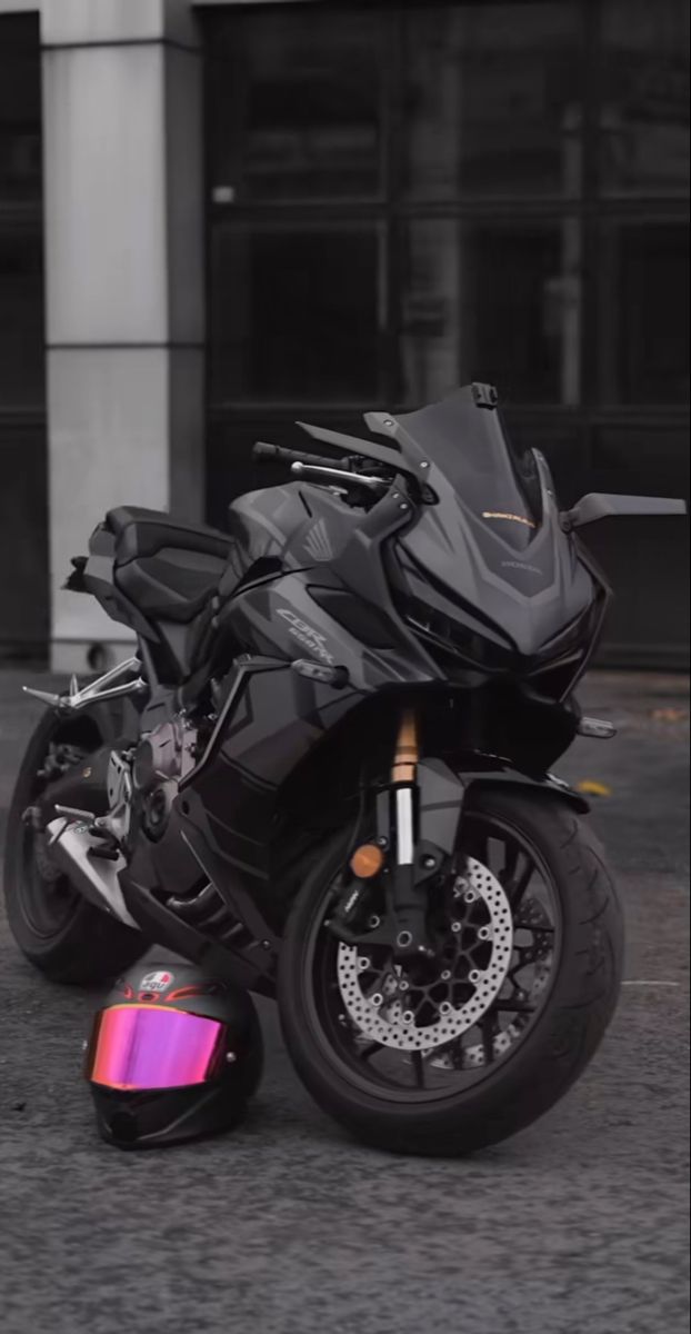 a black motorcycle parked next to a pink helmet on the ground in front of a building