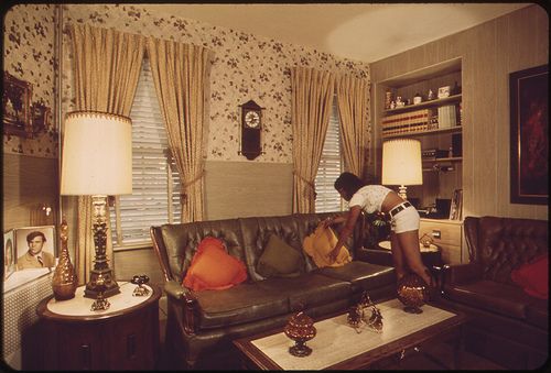 a woman is sitting on a couch in a living room with floral wallpaper and brown leather furniture