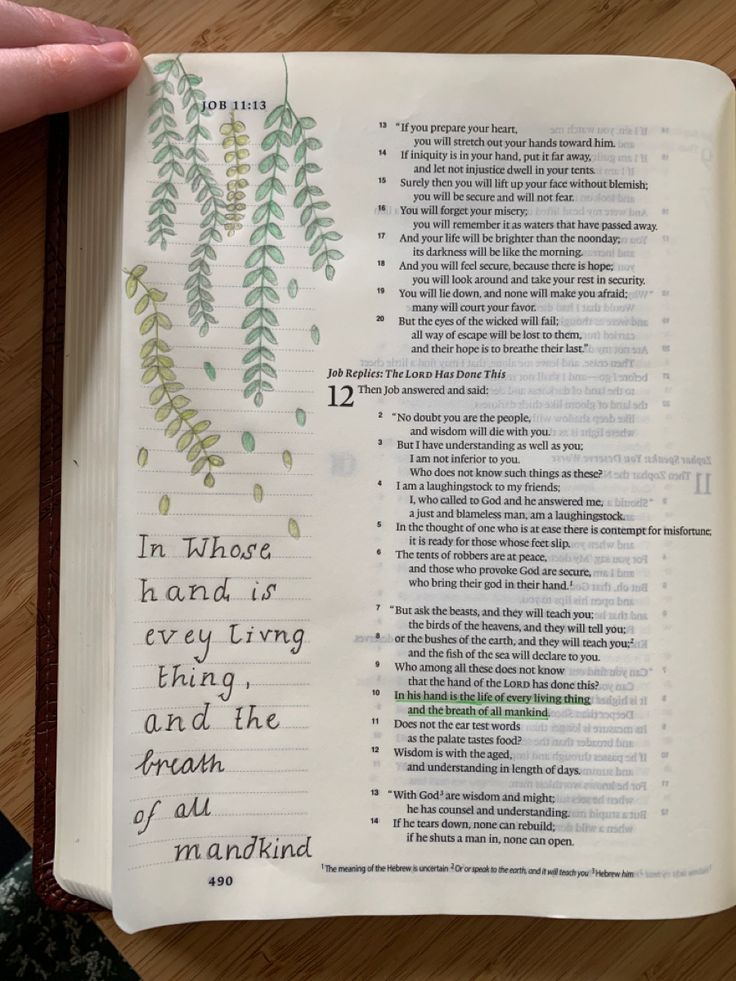 a hand holding an open bible on top of a wooden table with writing in it