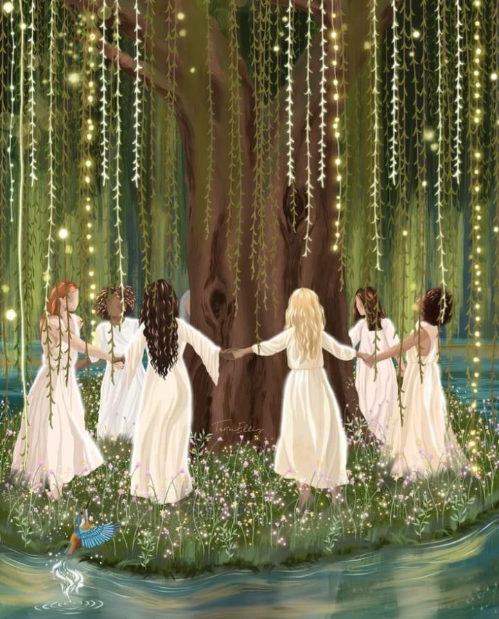 four girls in white dresses holding hands and walking through the water under a tree with lights hanging from it