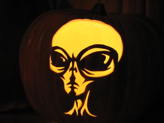 a carved pumpkin with an alien face on it's side and eyes glowing in the dark