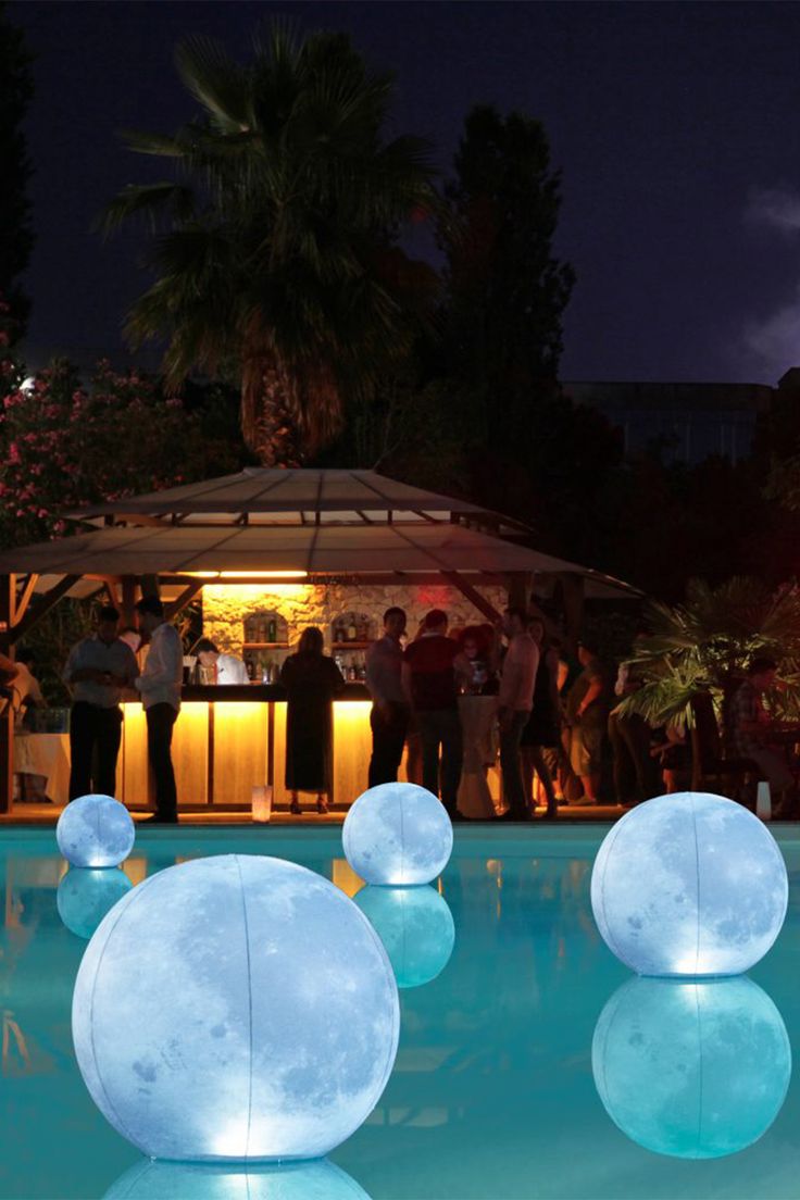 people are standing around in the pool at night with moon lights on it and water bubbles floating