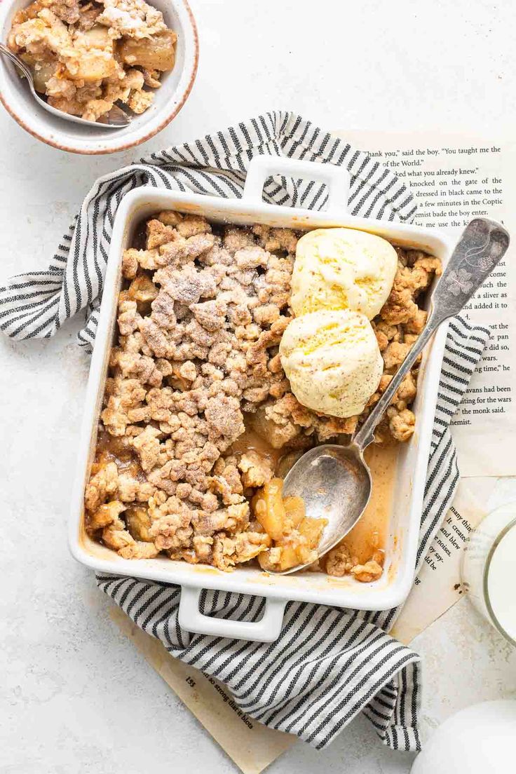 two bowls filled with apple crisp and ice cream on top of a striped napkin next to an open book