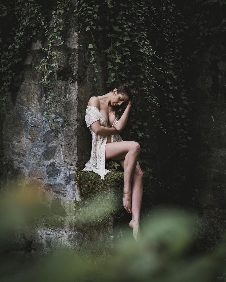 a woman sitting on top of a rock next to a lush green plant covered wall