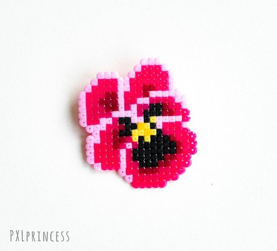 a pink and black beaded brooch sitting on top of a white surface