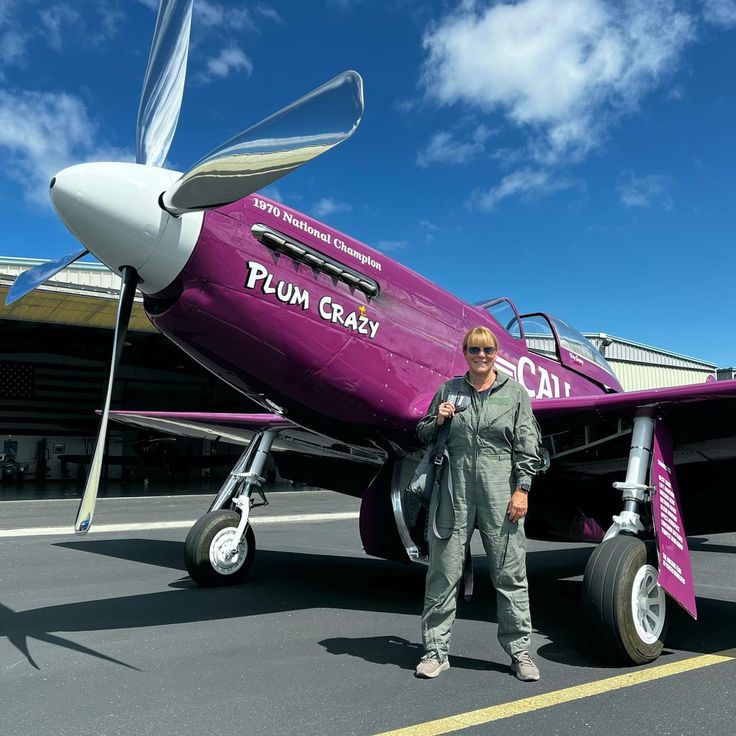 a woman standing in front of a purple plane on display at an air port hangar