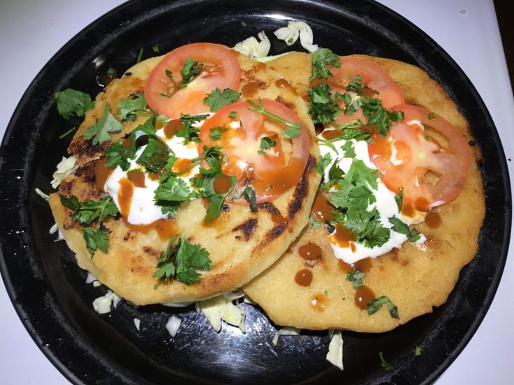 two flatbreads with tomatoes and sour cream on top are in a black pan