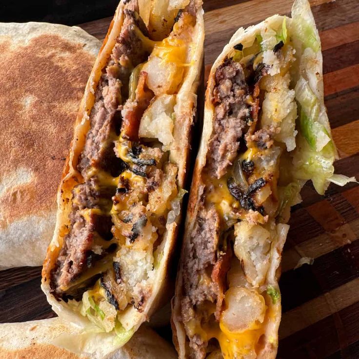 two sandwiches with meat, cheese and lettuce sitting on top of a cutting board