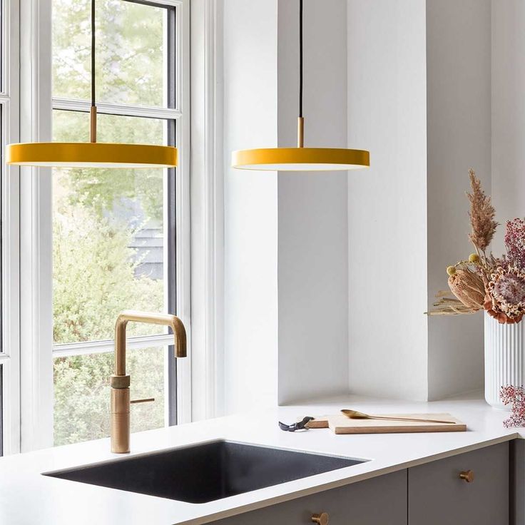 a kitchen with white counter tops and yellow pendant lights