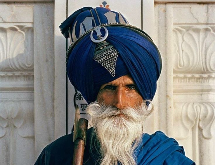 a man with a long white beard wearing a blue turban and holding a stick