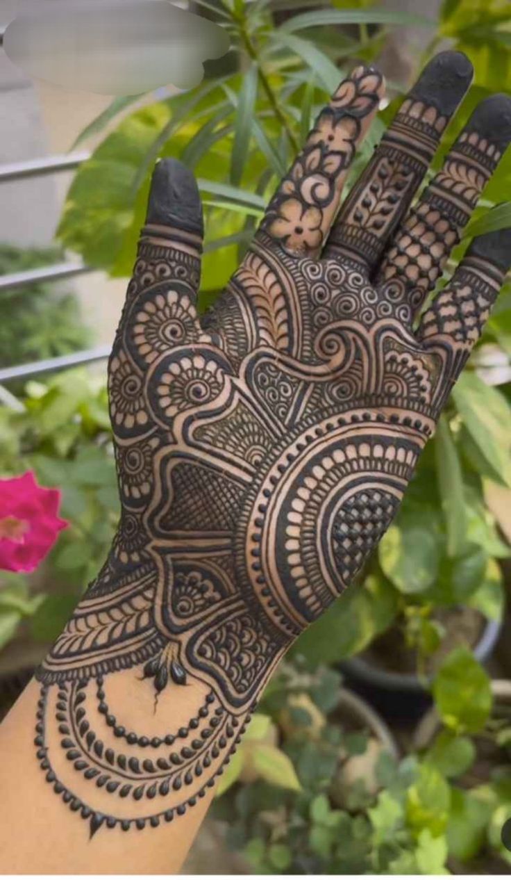 a hand with henna on it in front of some plants and flowers at the bottom