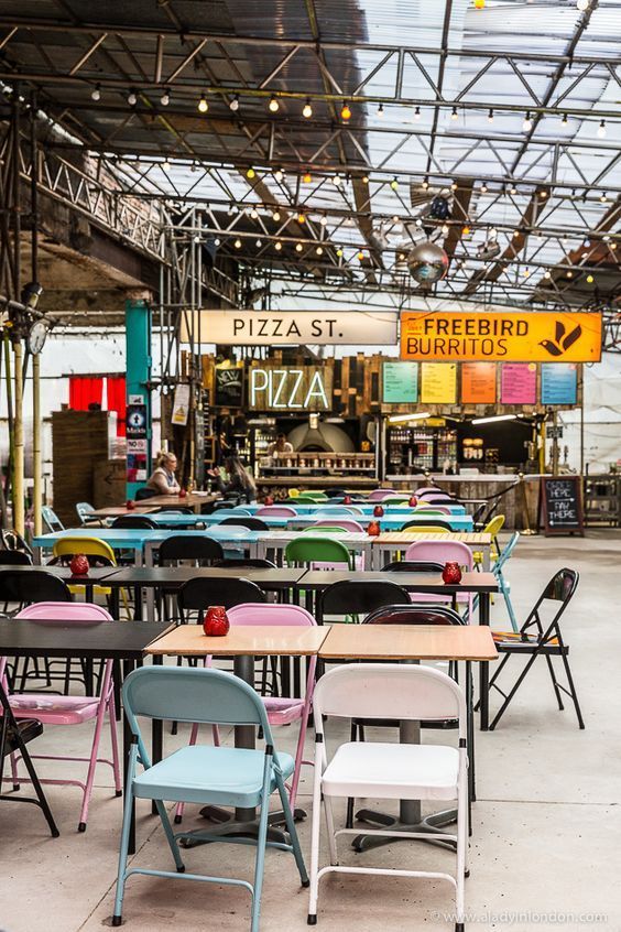 tables and chairs are lined up in an open area with signs on the wall above them