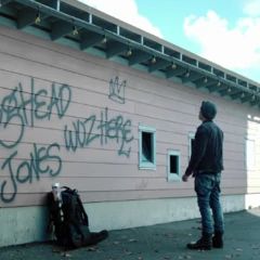 a man standing next to a building with graffiti on it's side and another person looking at the wall