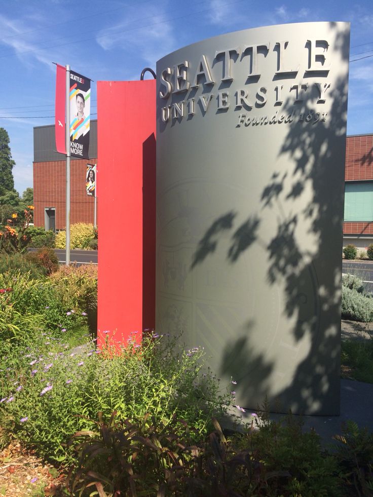 a large sign in front of a building with trees and bushes around it that says seattle university