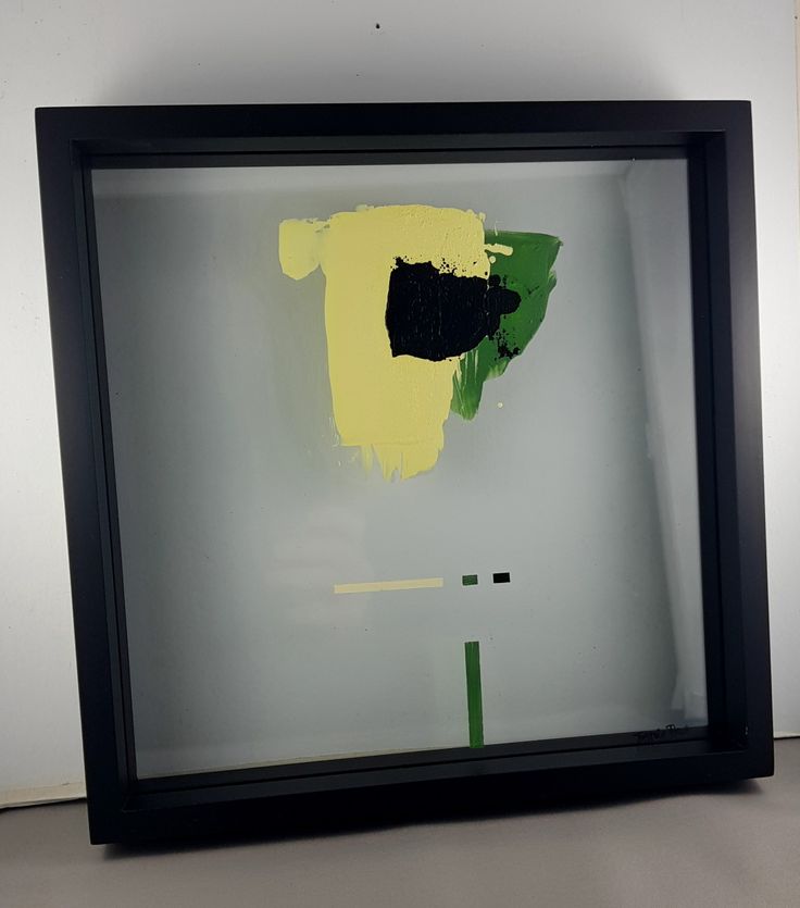 a black frame with yellow and green paint on it in front of a white wall