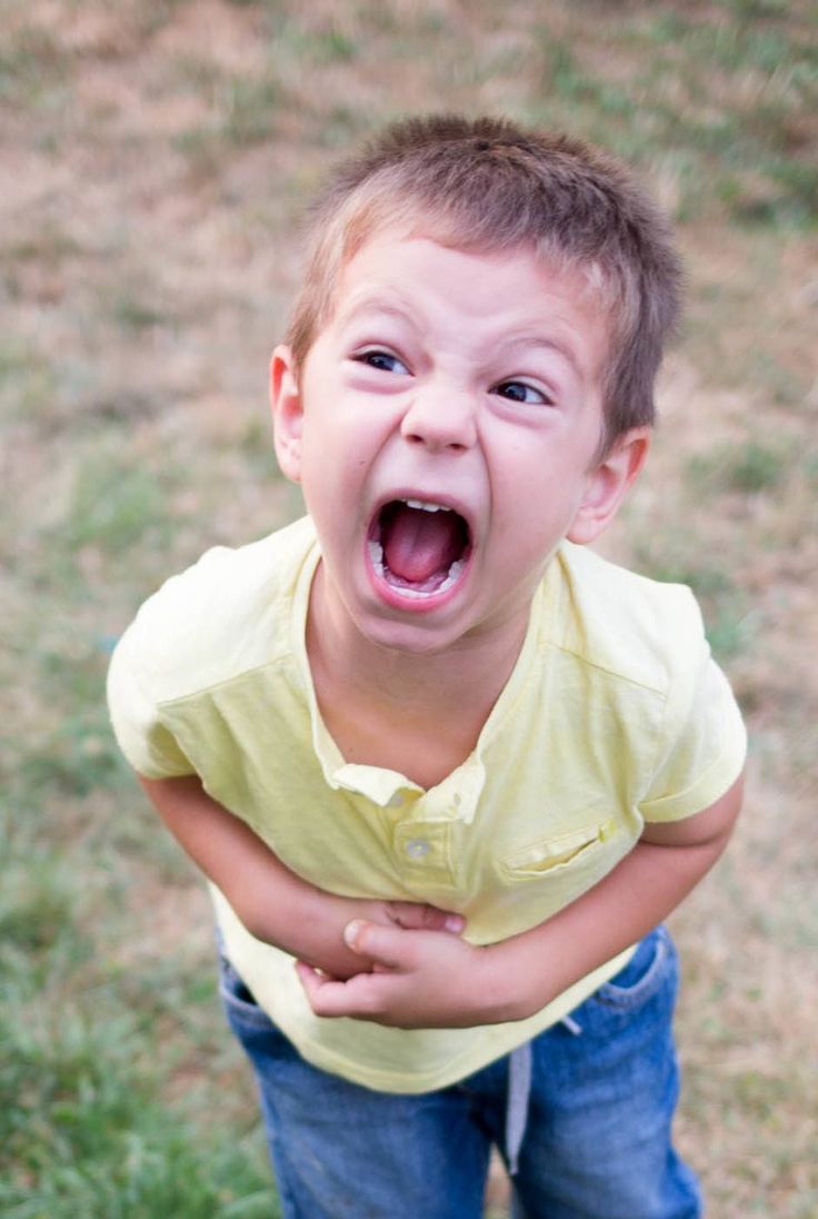 a young boy with his mouth open standing in the grass