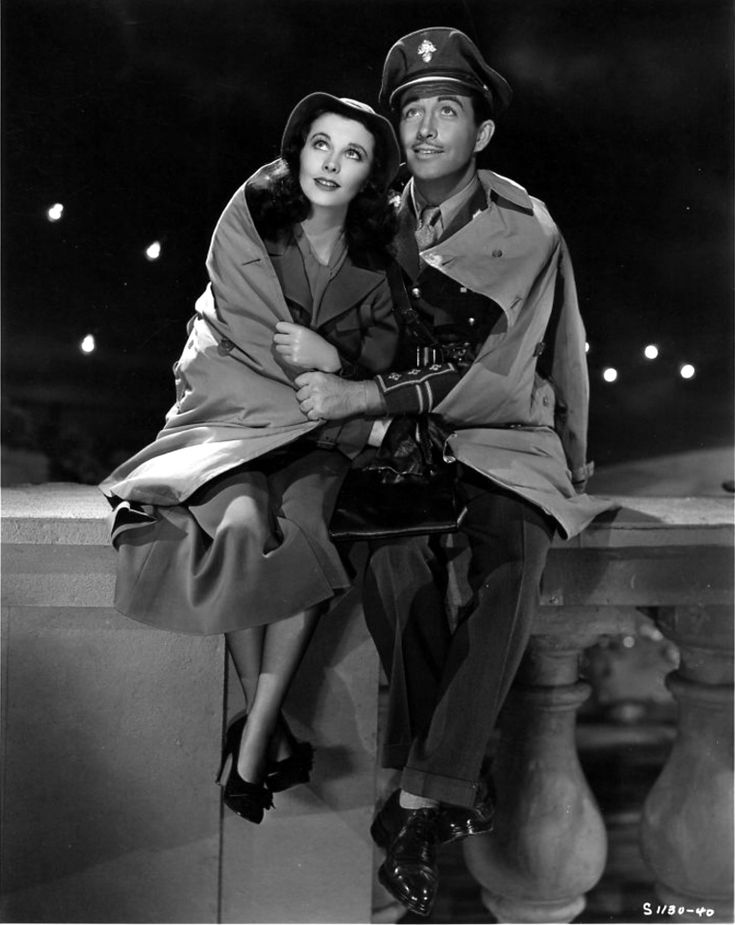 an old black and white photo of a man and woman sitting on a ledge with their arms around each other