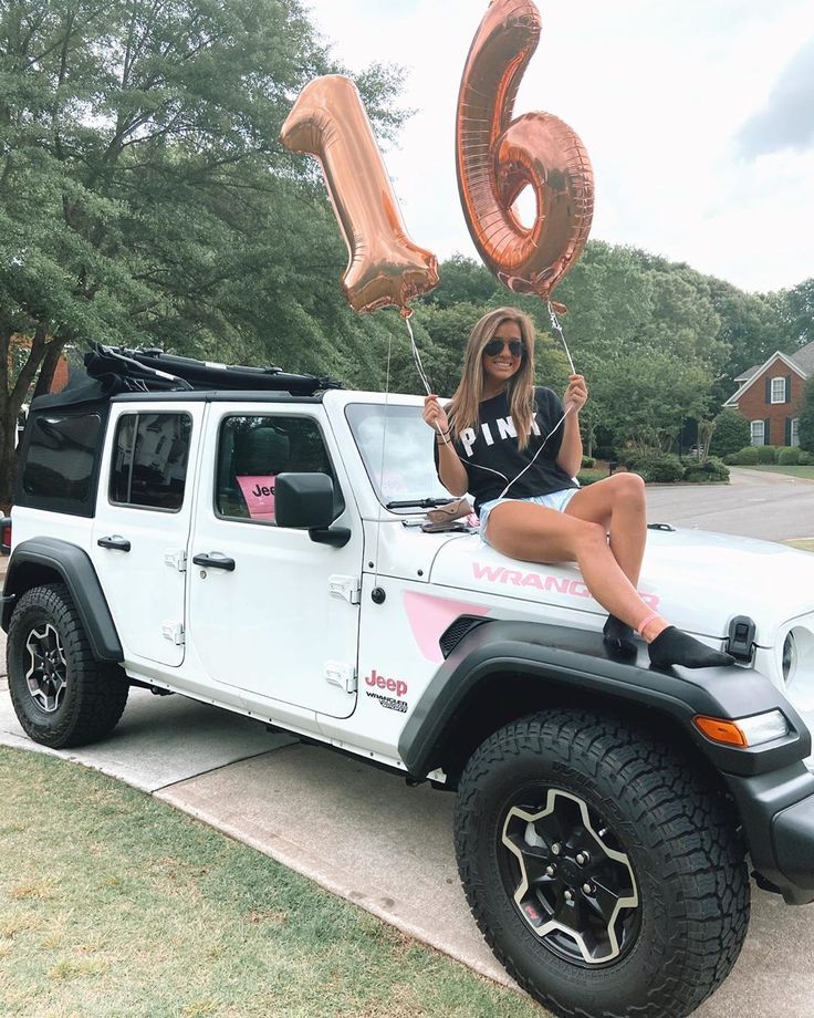 a woman sitting on the hood of a white jeep with balloons in the shape of numbers