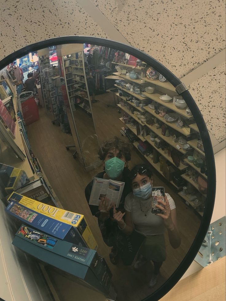 two people wearing masks are looking at books in a store through a mirror that is on the wall