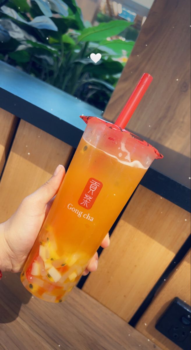 a person holding up a drink in front of a wall with plants and flowers on it