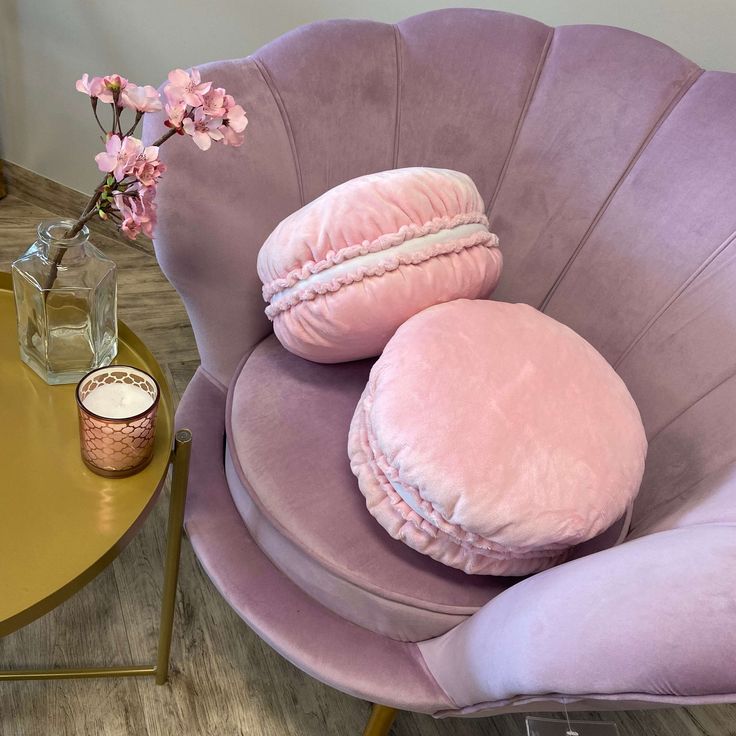 two round pillows sitting on top of a purple chair next to a vase with flowers