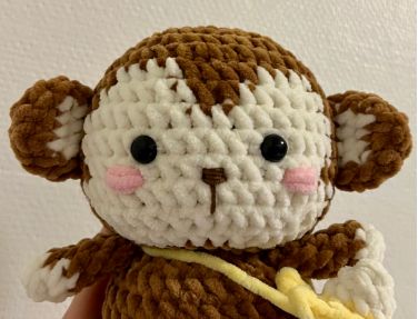 a crocheted monkey holding a banana in it's hand and wearing a yellow ribbon