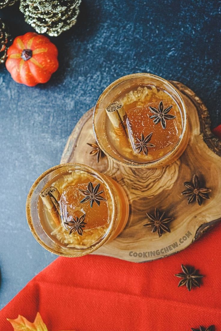 two glasses filled with liquid sitting on top of a wooden tray next to pumpkins