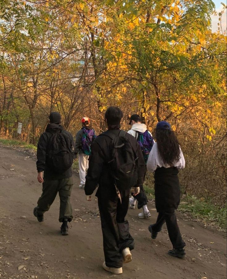 several people walking down a dirt road with backpacks on and trees in the background